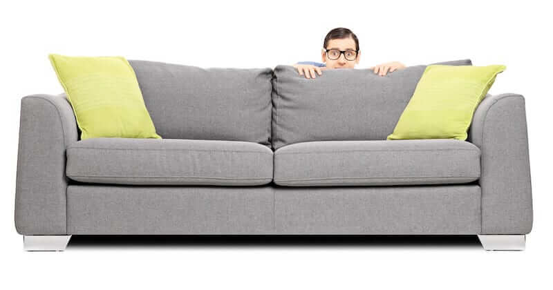 A man who is scared of the dentist is hiding behind the sofa