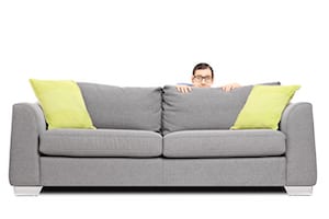 Scared man hiding behind a sofa